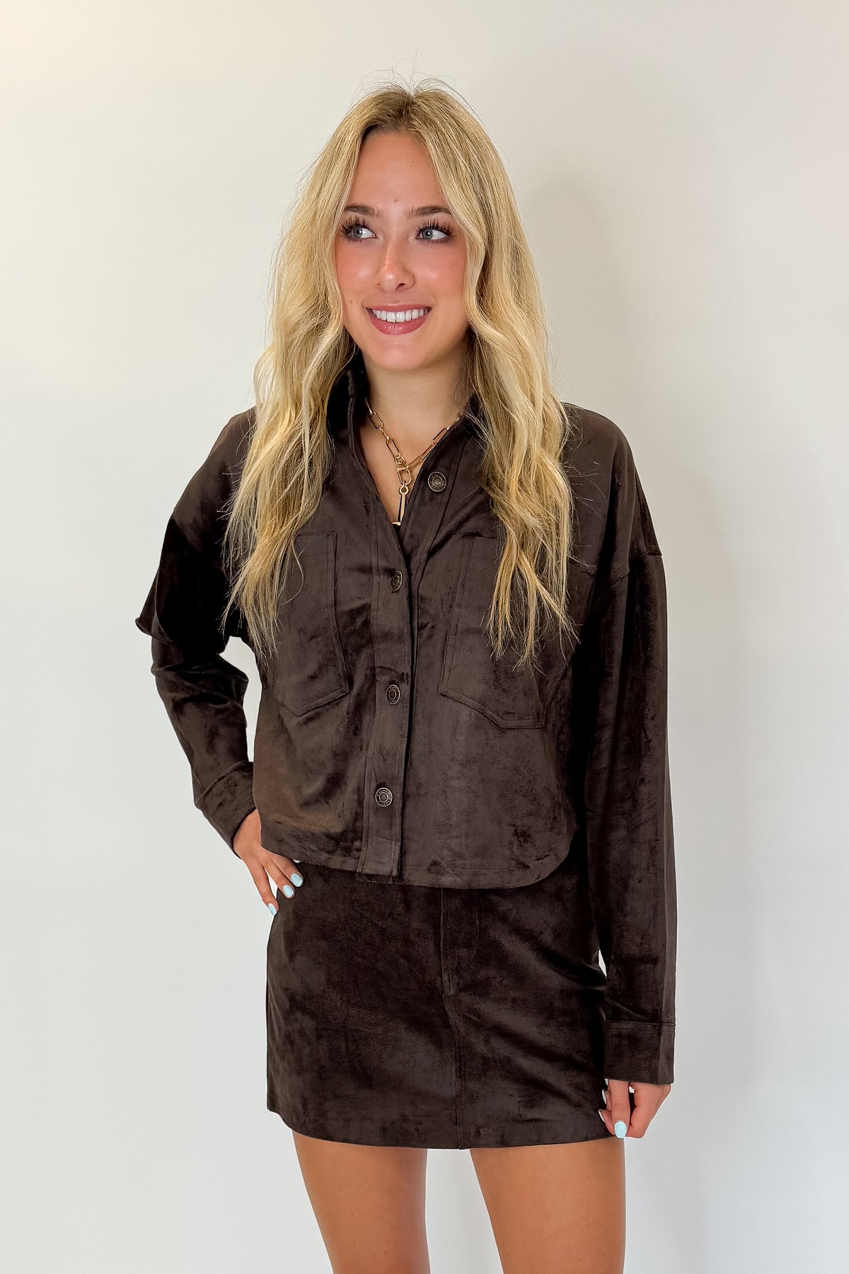 Front view of woman wearing Swagger Boutique’s All Day Cropped Suede Jacket and Perri Suede Mini Skirt by Z Supply In Dark Chocolate against white studio background.