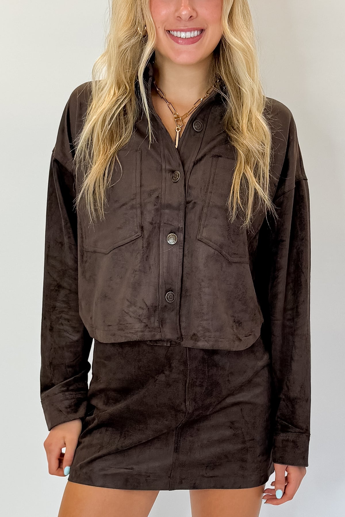 Front detail view of woman wearing Swagger Boutique’s All Day Cropped Suede Jacket and Perri Suede Mini Skirt by Z Supply In Dark Chocolate against white studio background.