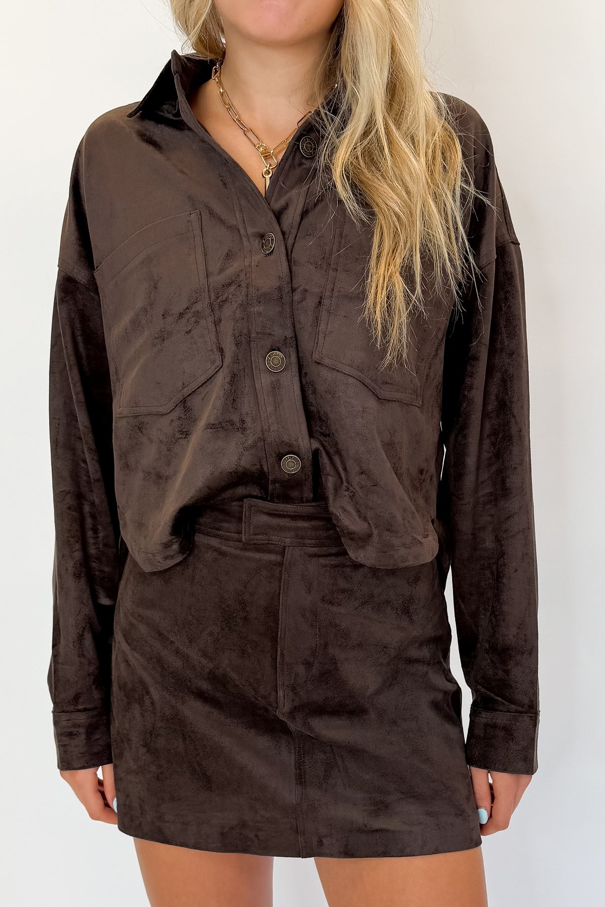 Front detail view of woman wearing Swagger Boutique’s All Day Cropped Suede Jacket and Perri Suede Mini Skirt by Z Supply In Dark Chocolate against white studio background.