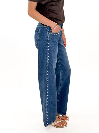 Side view of woman wearing Swagger Boutique’s Dark Wash Stud Jeans by Just Black Denim against white studio background.