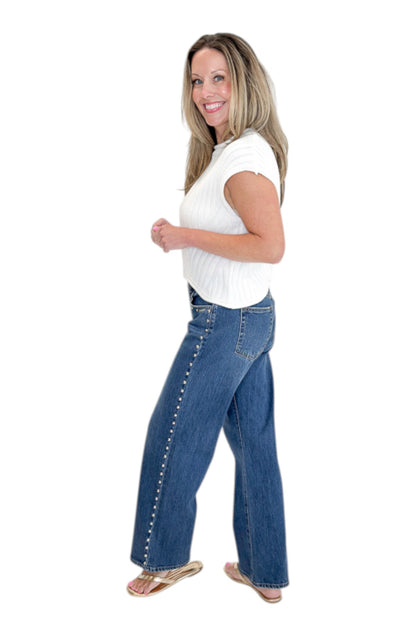Side view of woman wearing Swagger Boutique’s sweater with Dark Wash Stud Jeans by Just Black Denim against white studio background.