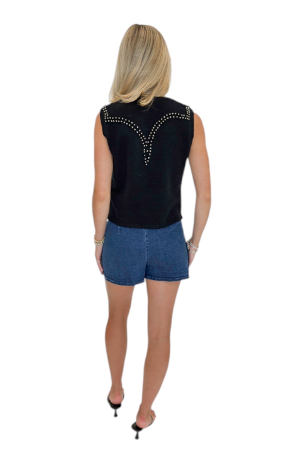 Back view of woman wearing Swagger Boutique’s Black Studded Sweater Vest with Dark Wash Studded Denim Skort against white studio background.