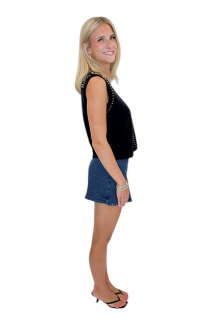 Side view of woman wearing Swagger Boutique’s Black Studded Sweater Vest with Dark Wash Studded Denim Skort against white studio background.
