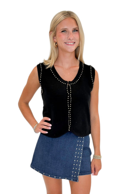 Front view of woman wearing Swagger Boutique’s Black Studded Sweater Vest with Dark Wash Studded Denim Skort against white studio background.