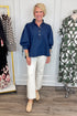 Front view of woman wearing Swagger Boutique’s Dark Wash Puff Sleeve Denim Top by Entro with jeans with clothing hanging in the background.