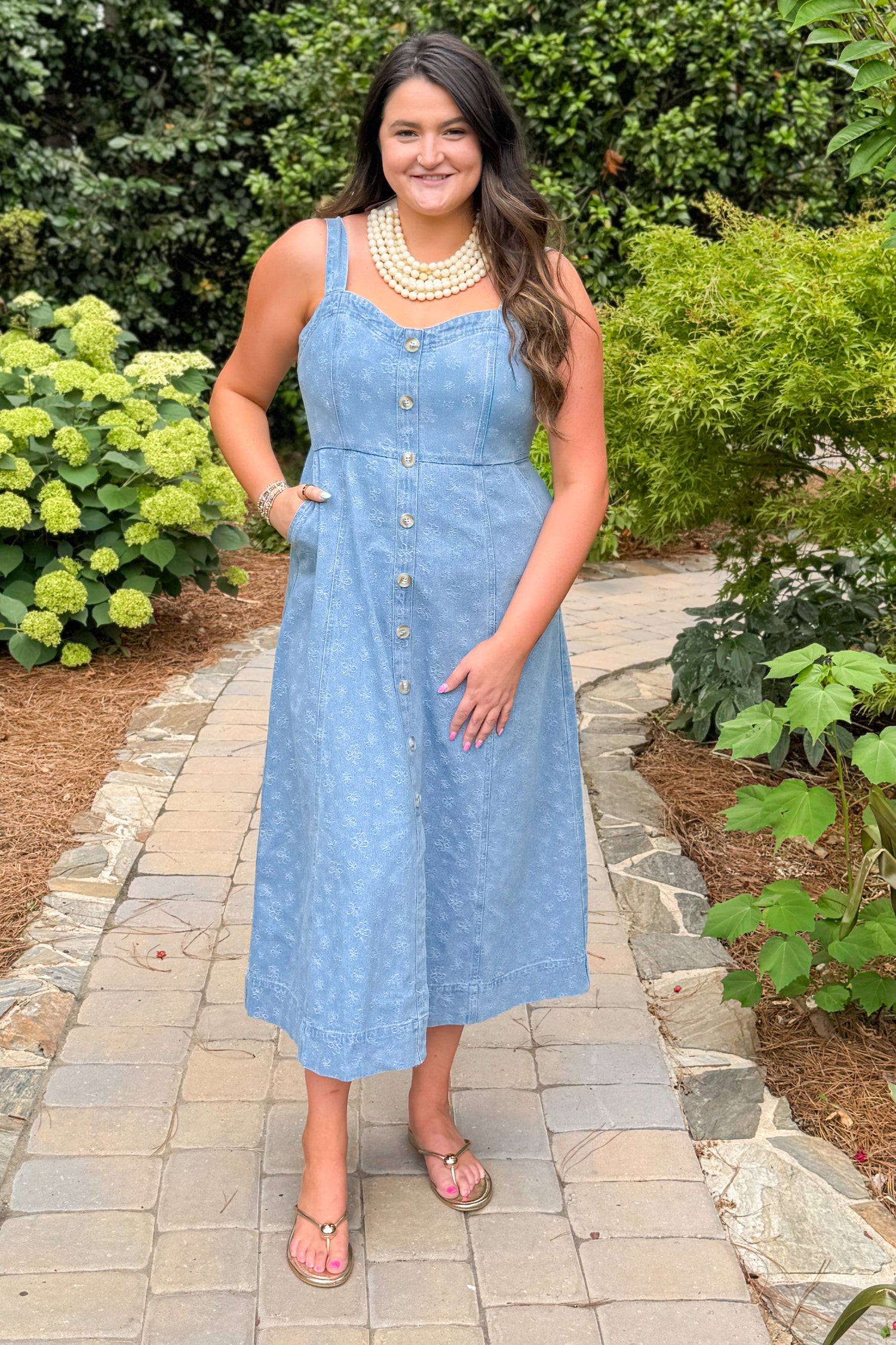 Front view of woman wearing Swagger Boutique’s Denim Floral Textured Midi Dress with sandals walking down a path.