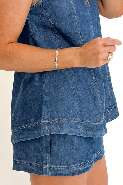Side detail view of woman wearing Swagger Boutique’s Denim Seam Detail Swing Tank with matching Denim Seam Detail Shorts against white studio background.