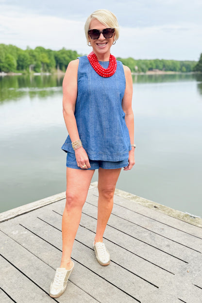 Front view of woman wearing Swagger Boutique’s Denim Seam Detail Swing Tank with matching Denim Seam Detail Shorts and sneakers outside at the lake.