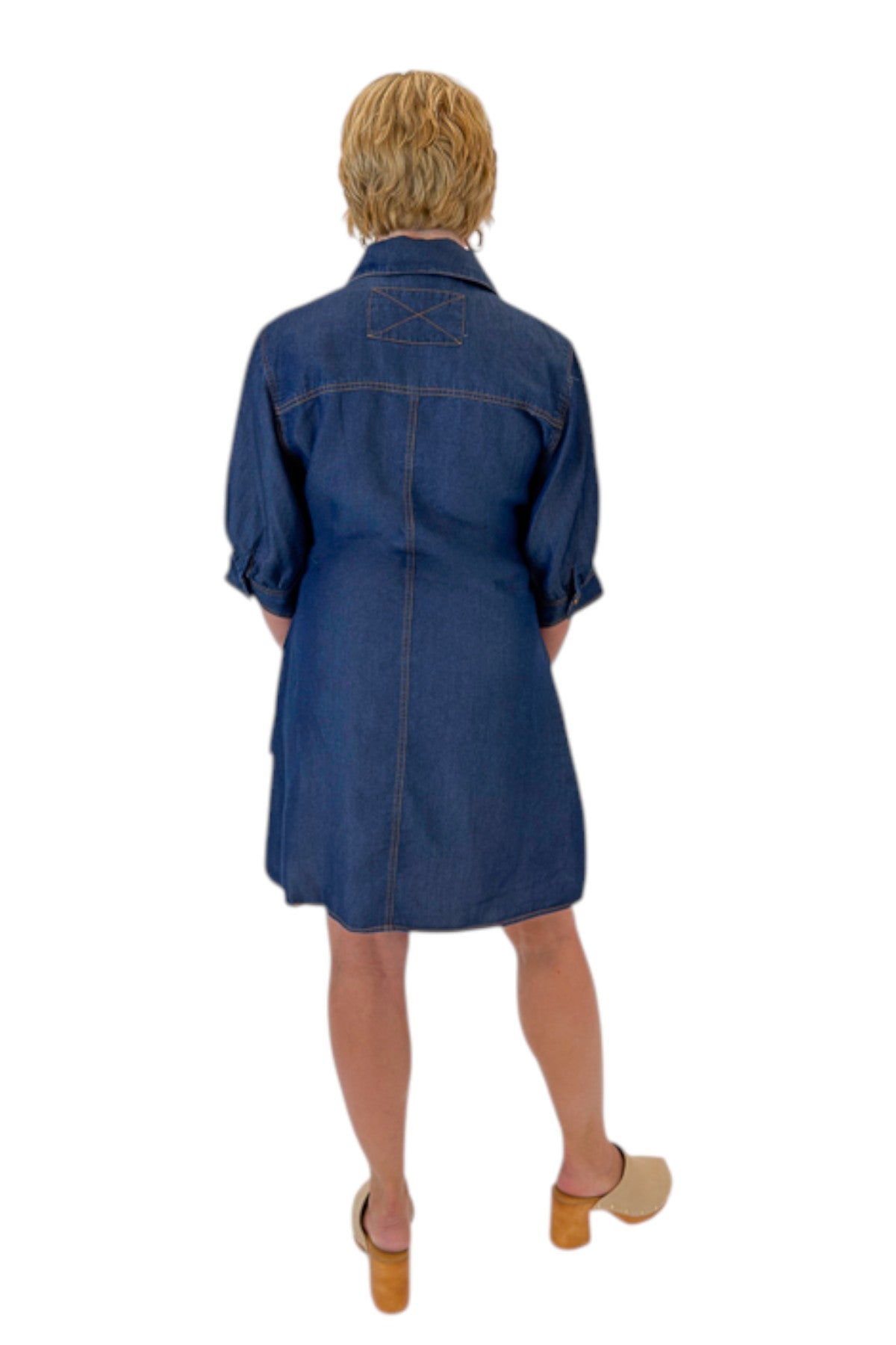 Back view of woman wearing Swagger Boutique’s Denim Tie Detail Button Up Dress by Entro with clogs against white studio background.