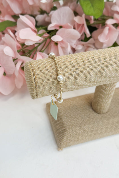 Gold bracelet on a beige stand against a pink floral background