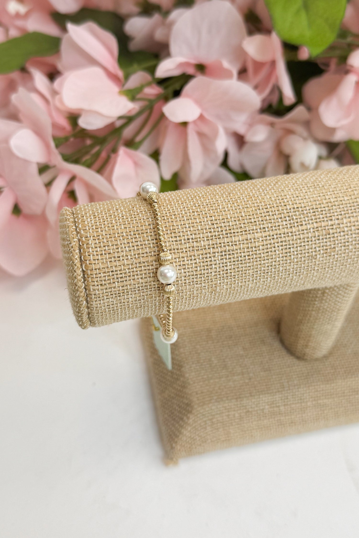 Gold bracelet on a beige stand against a pink floral background