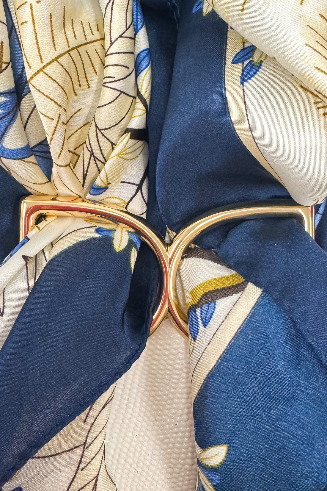Gold-tone scarf ring enhancer securing a blue and white patterned scarf, shown in a close-up