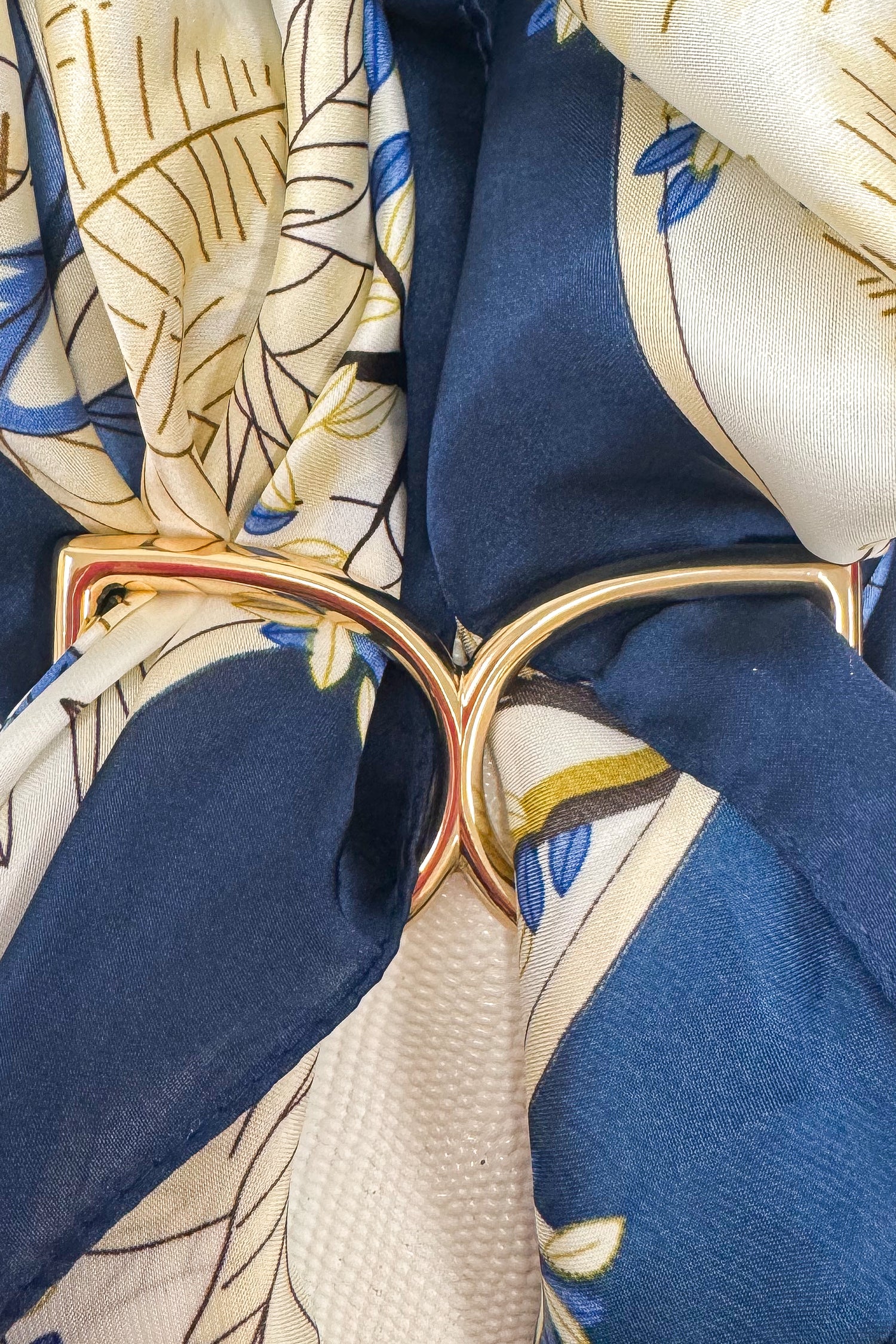 Gold-tone scarf ring enhancer securing a blue and white patterned scarf, shown in a close-up