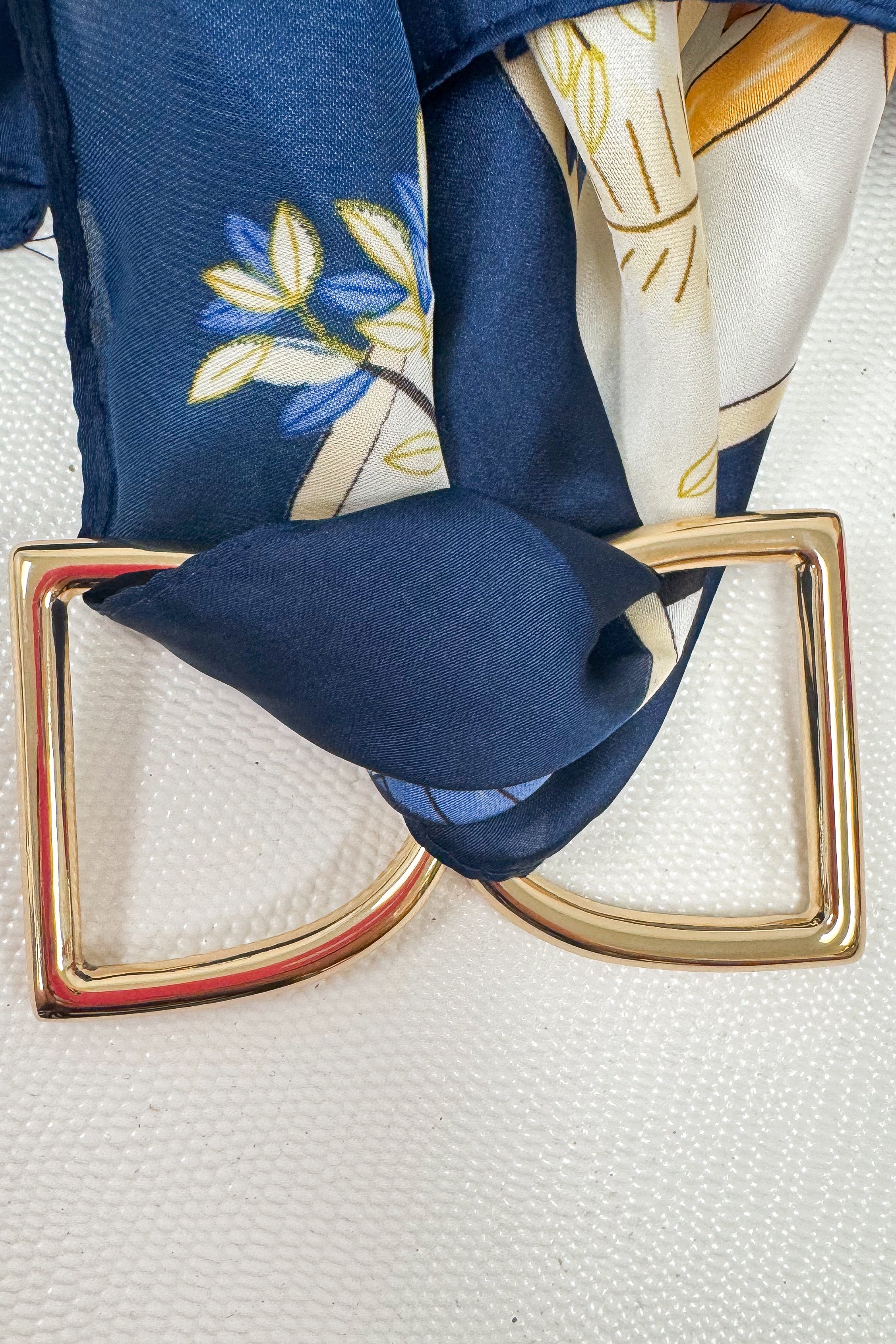 Gold-tone scarf ring enhancer styled on a blue and white patterned scarf, showing the ring holding the scarf in place on a white studio background
