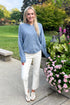 Front view of woman wearing Swagger Boutique’s Dusty Blue Button Up Cardigan with jeans standing outside by flowers. 