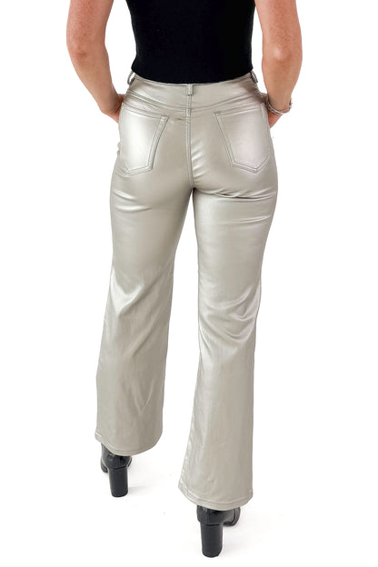 Back view of woman wearing silver coated jeans black top against white studio background.