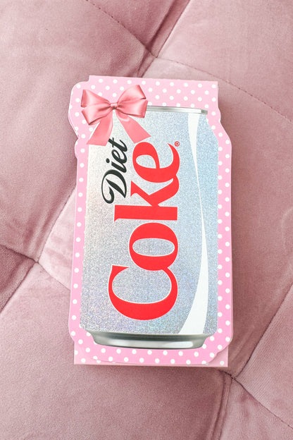 Diet Coke can-shaped pocket notepad with pink polka dot border and bow on a pink textured background