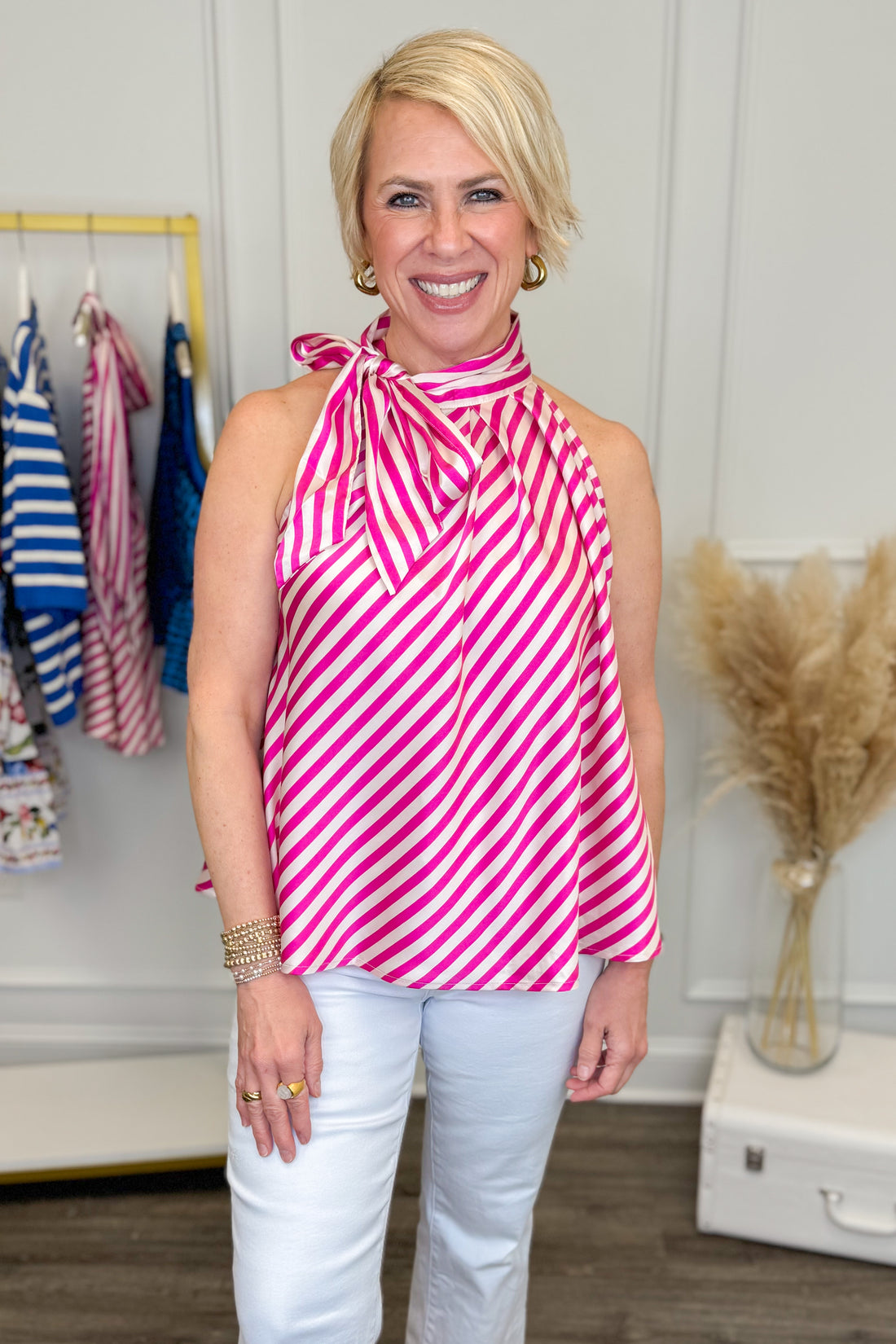 Woman wearing Pink Striped Halter Tie Neck Tank with white jeans with clothes in the background.