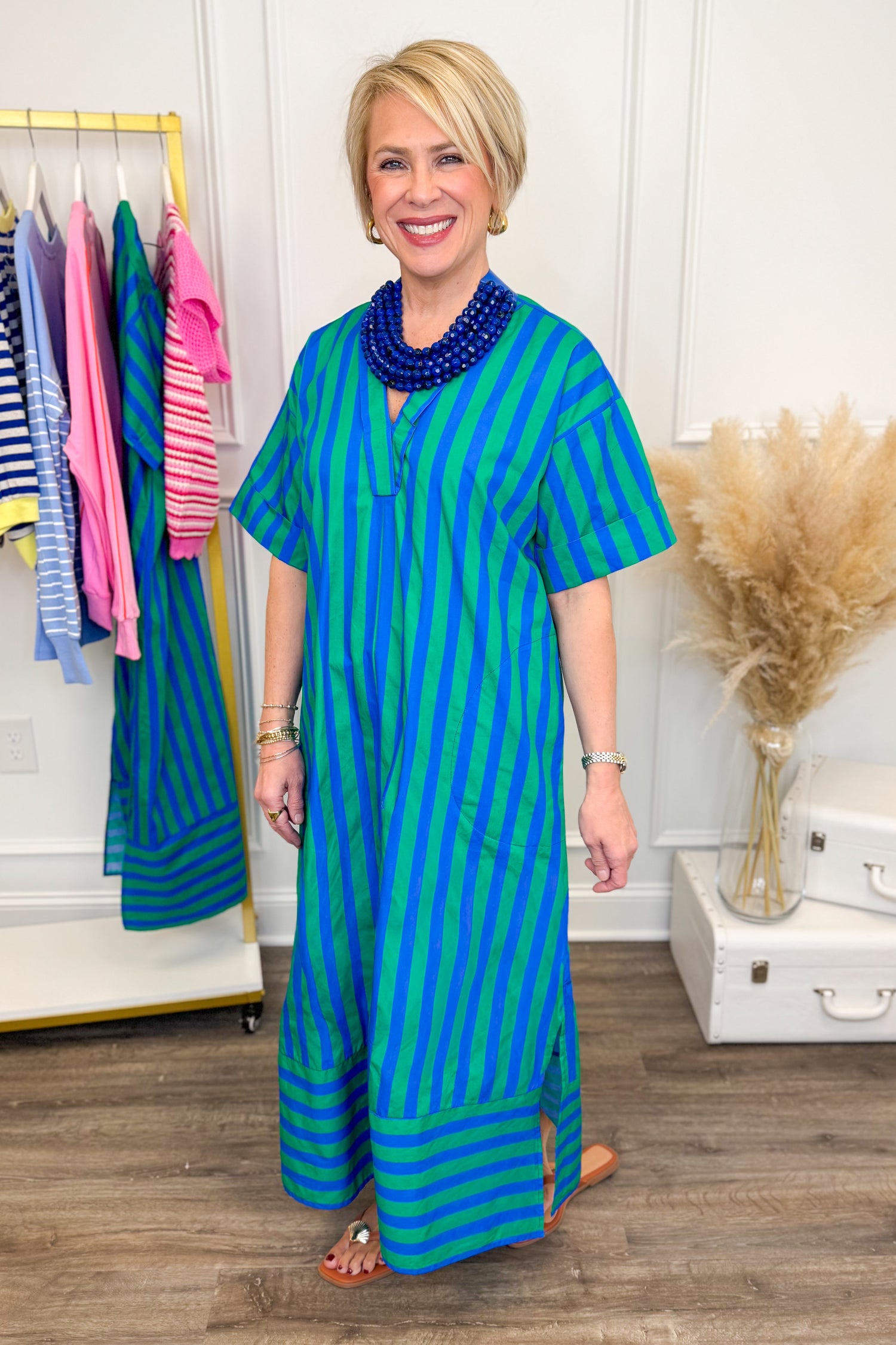 Side view of woman wearing striped dress with blue necklace with clothes in background.