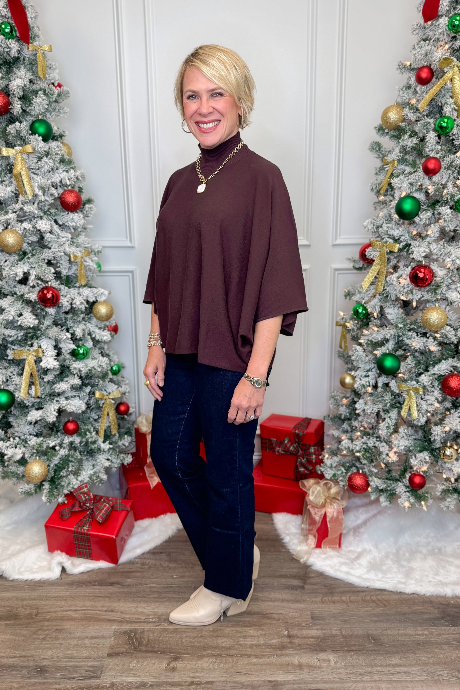 Woman standing in front of two decorated Christmas trees with presents.