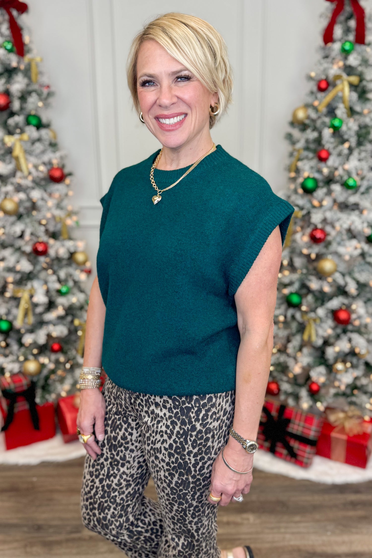 Woman in green top and leopard print pants standing in front of Christmas trees.
