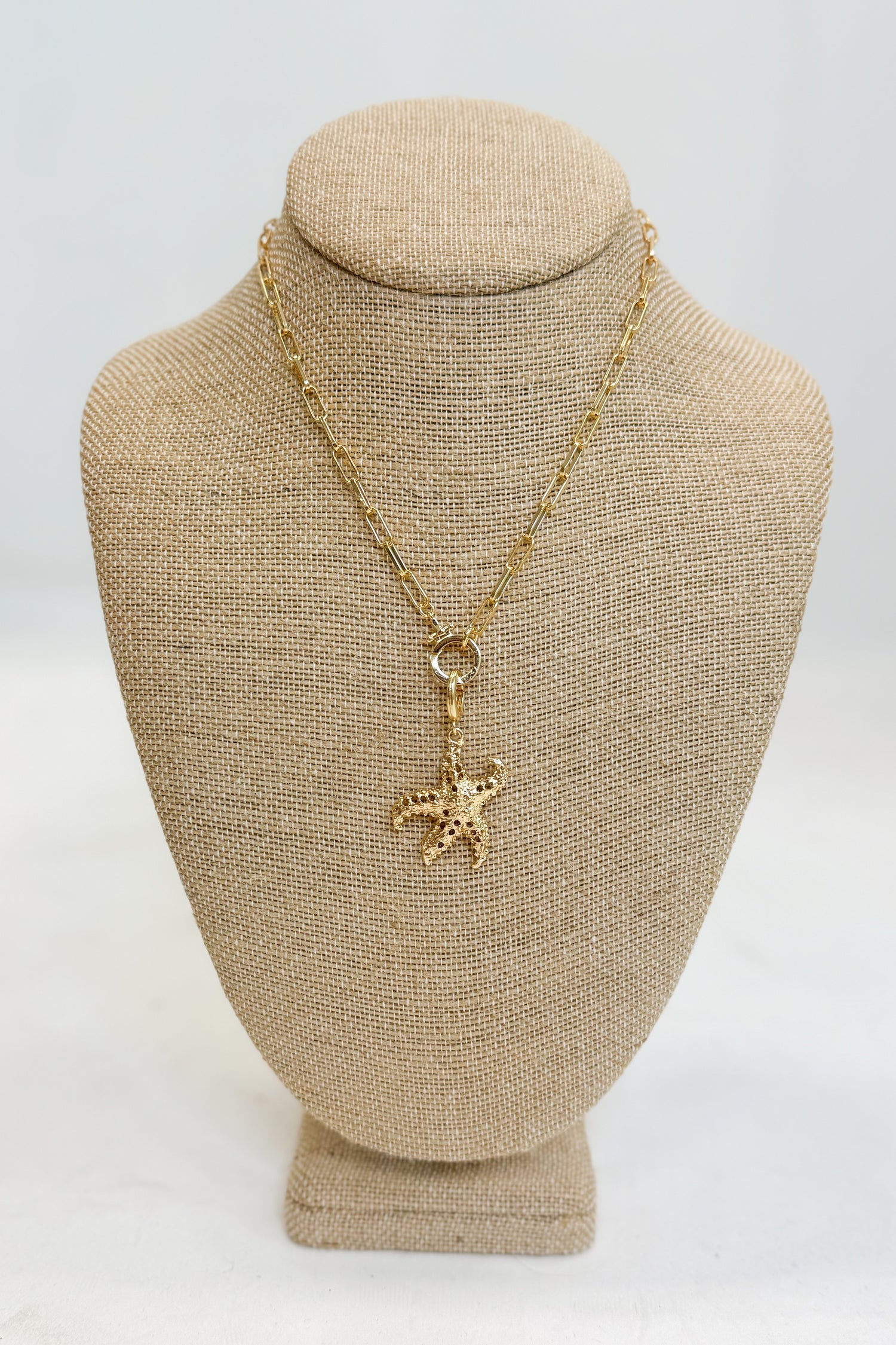 Gold necklace with a starfish pendant on a beige bust against a white background