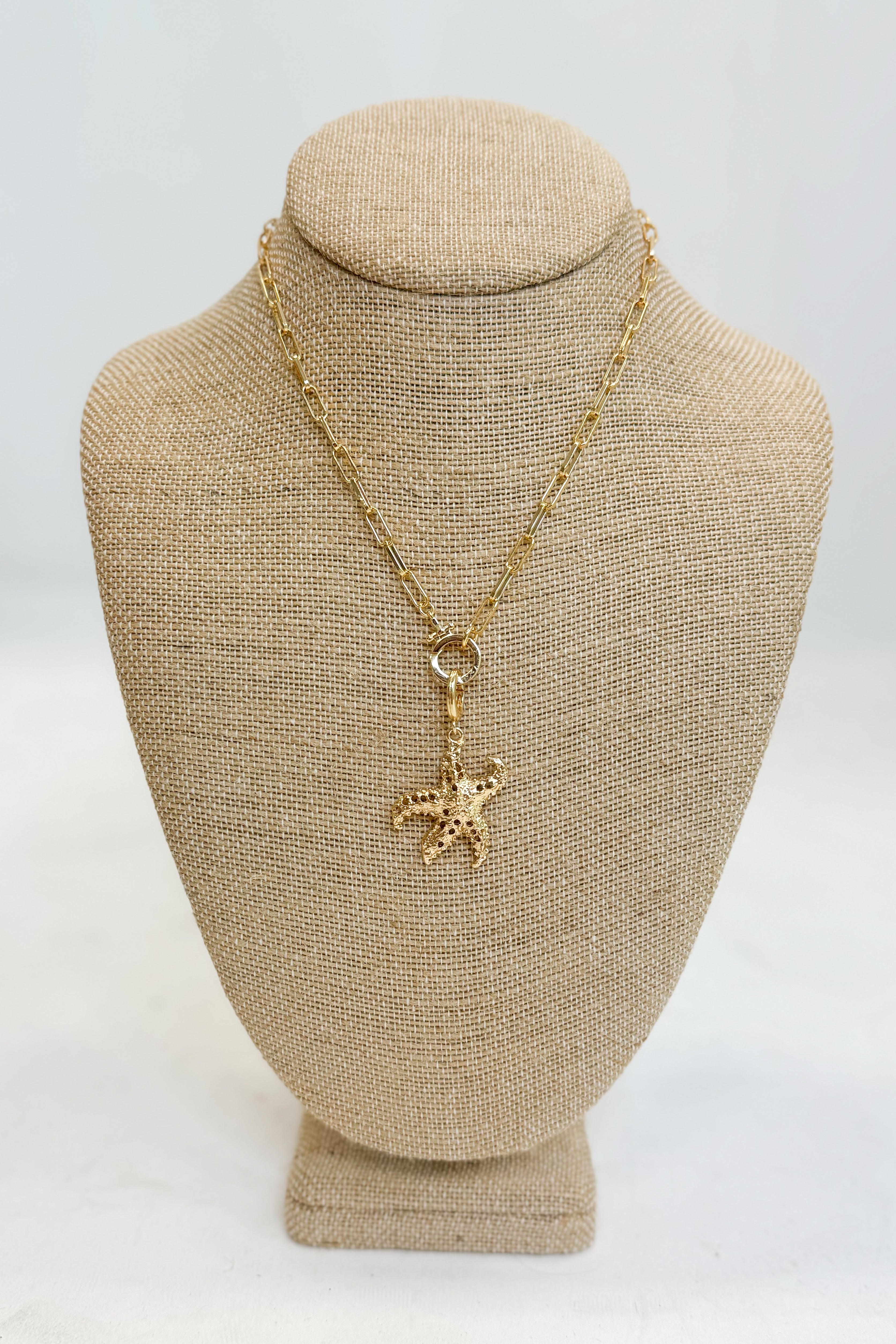 Gold necklace with a starfish pendant on a beige bust against a white background