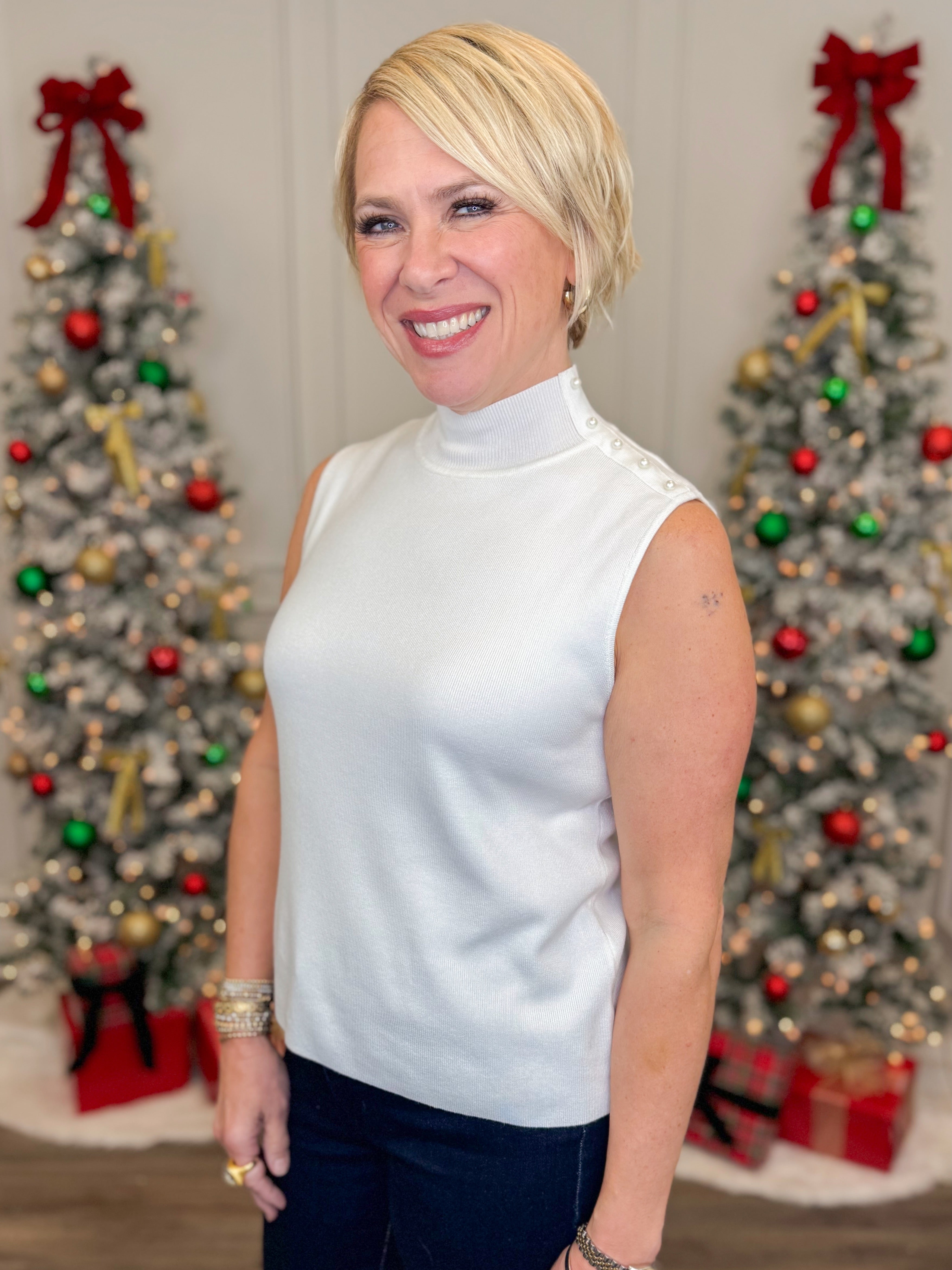 Front view of woman wearing Off White Pearl Detail Mock Neck Top and jeans with holiday decor in the background.