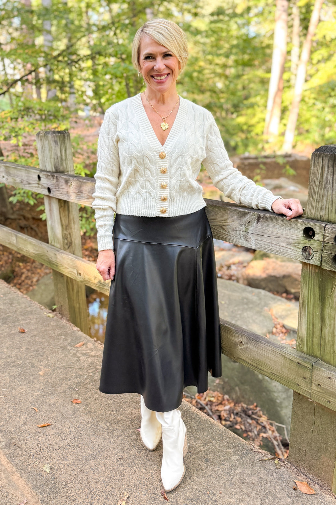 Woman outside on walk way wearing cream sweater with black faux leather skirt.