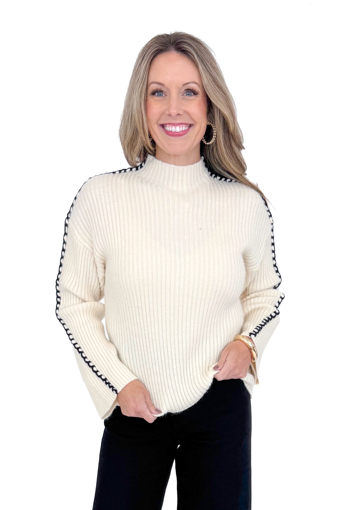 Front view of woman wearing cream sweater with jeans against white studio background.