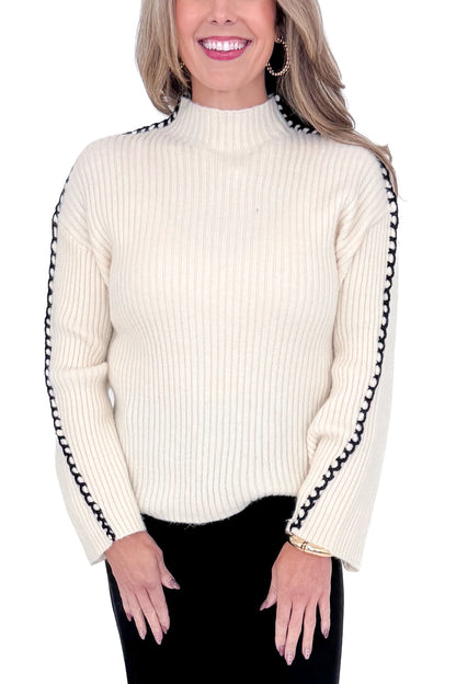 Front detailed view of woman wearing cream sweater with jeans against white studio background.