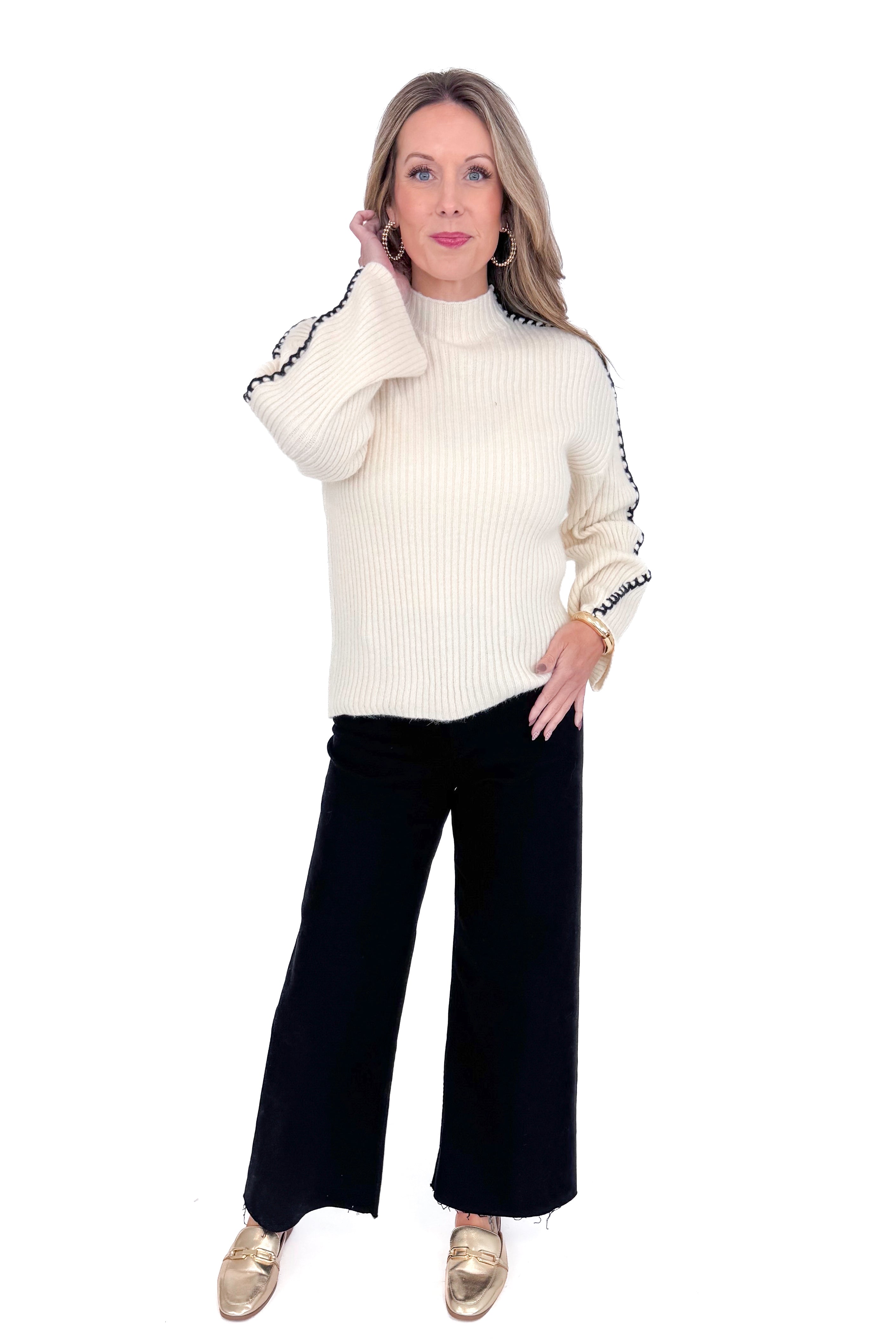 Front view of woman wearing cream sweater with jeans against white studio background.
