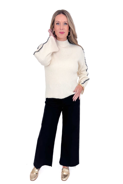 Front view of woman wearing cream sweater with jeans against white studio background.