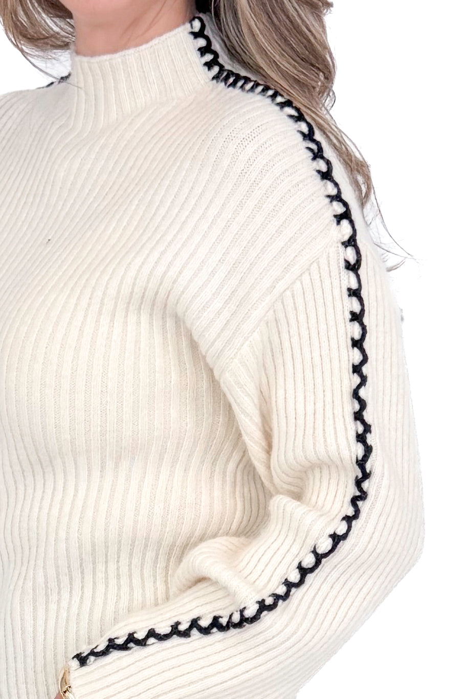 Side detailed view of woman wearing cream sweater with jeans against white studio background.