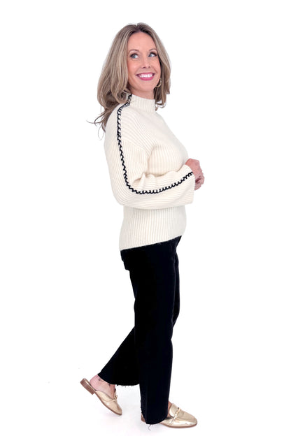 Side view of woman wearing cream sweater with jeans against white studio background.