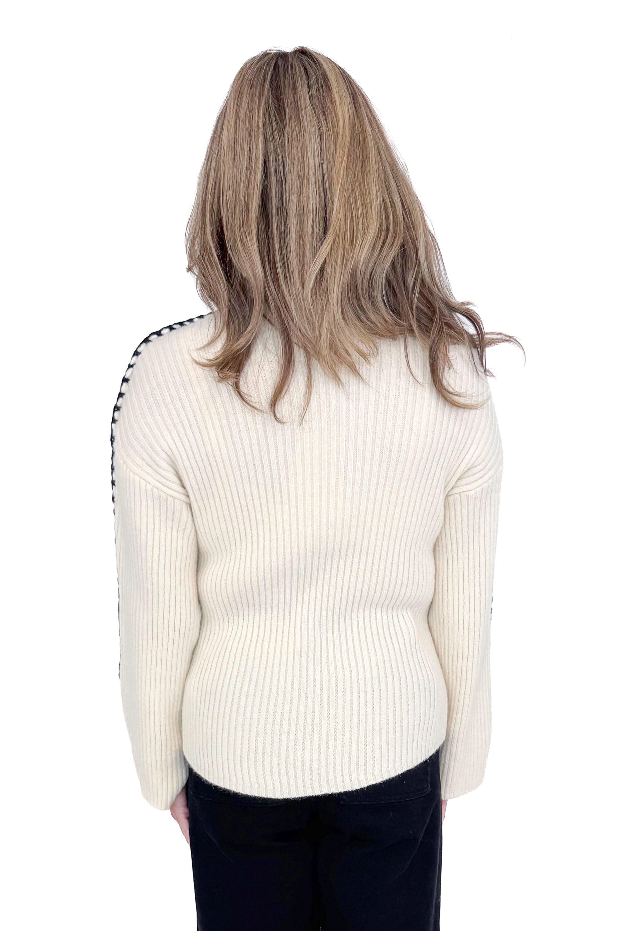 Back view of woman wearing cream sweater with jeans against white studio background.