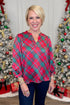 Woman wearing a red and green plaid top in front of Christmas trees.