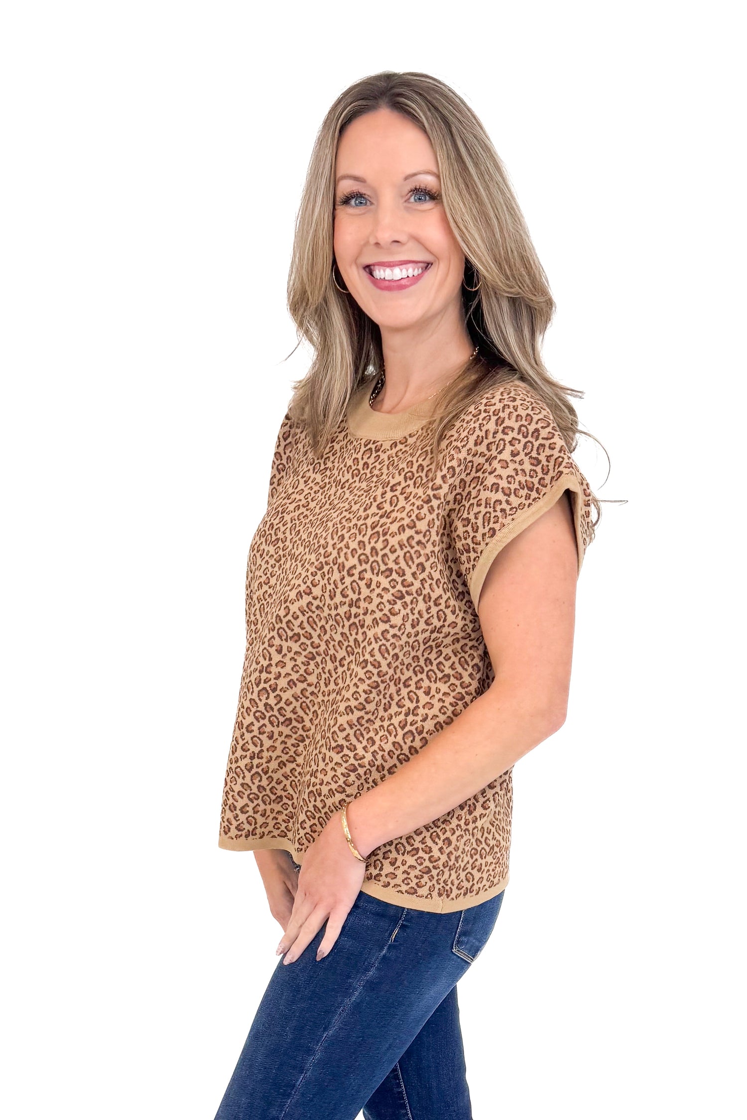 Side view of woman wearing leopard top with jeans against white studio background.
