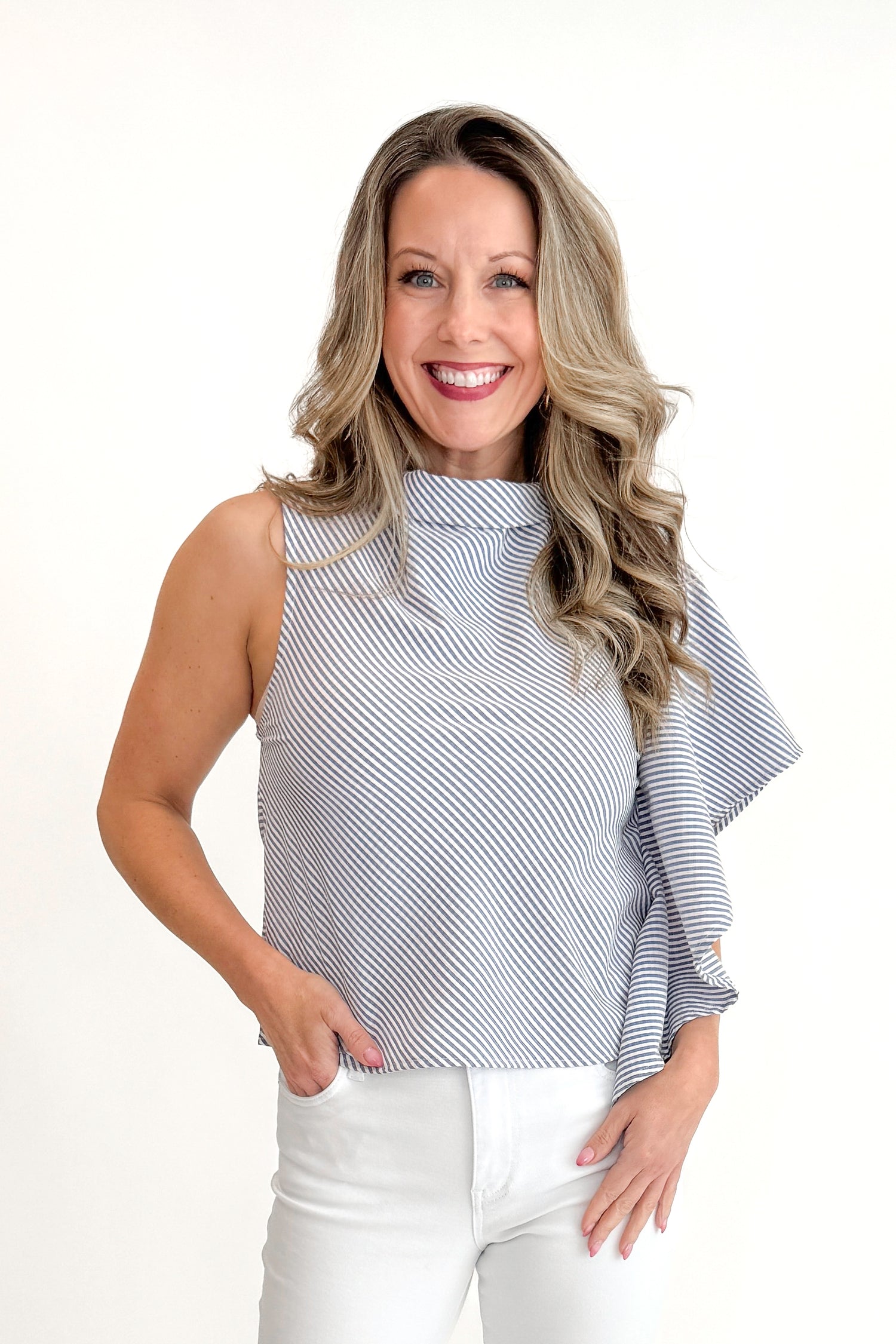 Front view of woman wearing Navy &amp; Ivory Striped Asymmetrical Ruffle Top with jeans and gold bar sandals against white studio background.