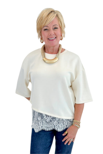Front view of woman wearing Swagger Boutique’s Ecru Asymmetrical Lace Hem Top by Entro with jeans against white studio background.