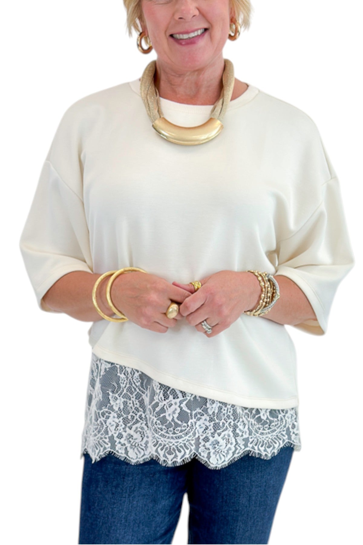 Front detail view of woman wearing Swagger Boutique’s Ecru Asymmetrical Lace Hem Top by Entro with jeans against white studio background.
