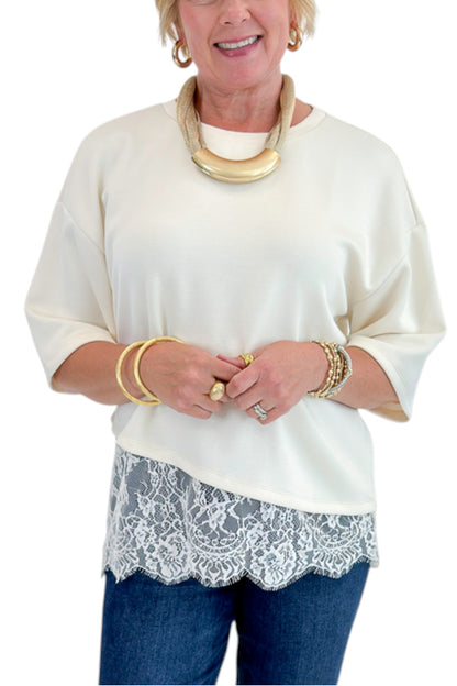 Front detail view of woman wearing Swagger Boutique’s Ecru Asymmetrical Lace Hem Top by Entro with jeans against white studio background.