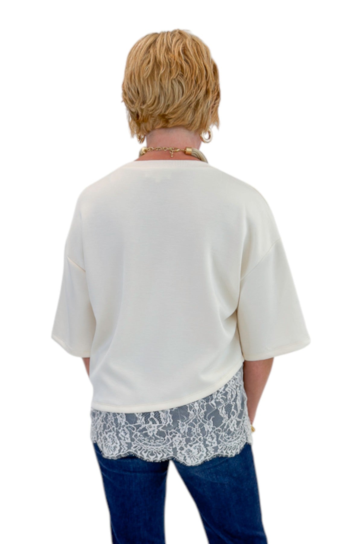 Back view of woman wearing Swagger Boutique’s Ecru Asymmetrical Lace Hem Top by Entro with jeans against white studio background.
