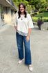 Front view of woman wearing Swagger Boutique’s Ecru Asymmetrical Lace Hem Top by Entro with jeans standing outside.
