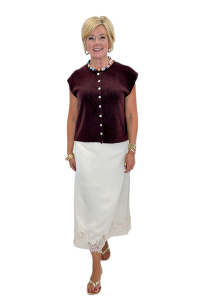 Front view of woman wearing Swagger Boutique’s Wine Sleeveless Button Up Sweater with Ecru Lace Lined Satin Skirt by Entro against white studio background.