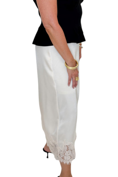 Side view of woman wearing Swagger Boutique’s black top with Ecru Lace Lined Satin Skirt by Entro against white studio background.