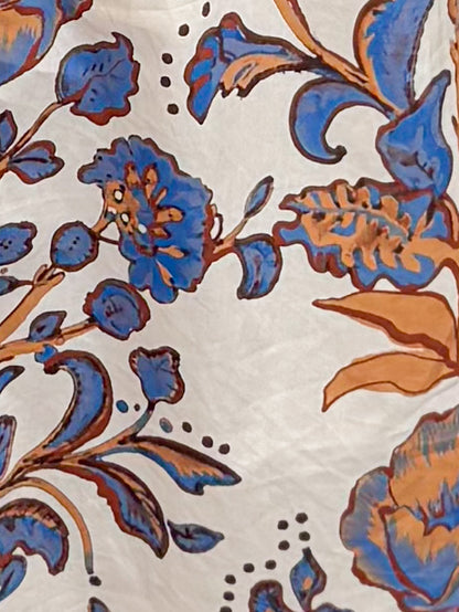 A close-up of a fabric featuring blue and orange floral motifs on a warm off-white background.