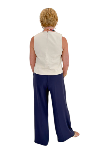 Back view of woman wearing Swagger Boutique’s Ecru Horsebit Buckle Tank by Entro with Navy High Waisted Trousers by Skies Are Blue against white studio background.