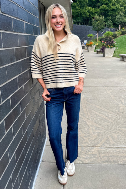 Front view of woman wearing Swagger Boutique’s Ecru &amp; Navy Striped 3/4 Sleeve Sweater by Entro with jeans leaning against a wall outside.