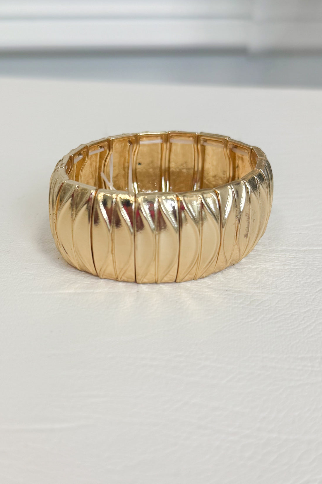 Gold-tone textured bracelet featuring a repeating detailed pattern across the band on a white studio background